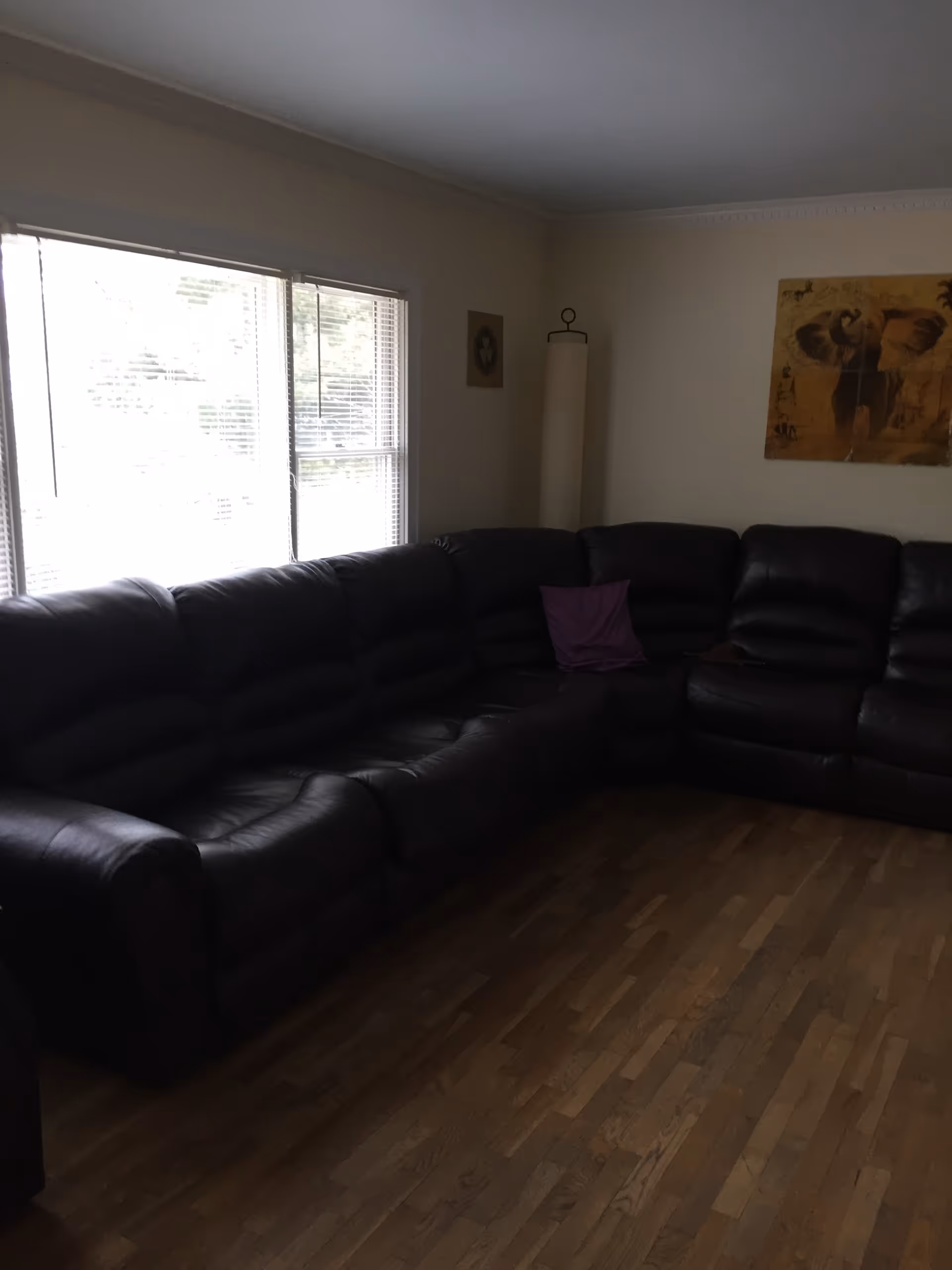 Large dark leather sectional sofa along a windowed living room with wall art.
