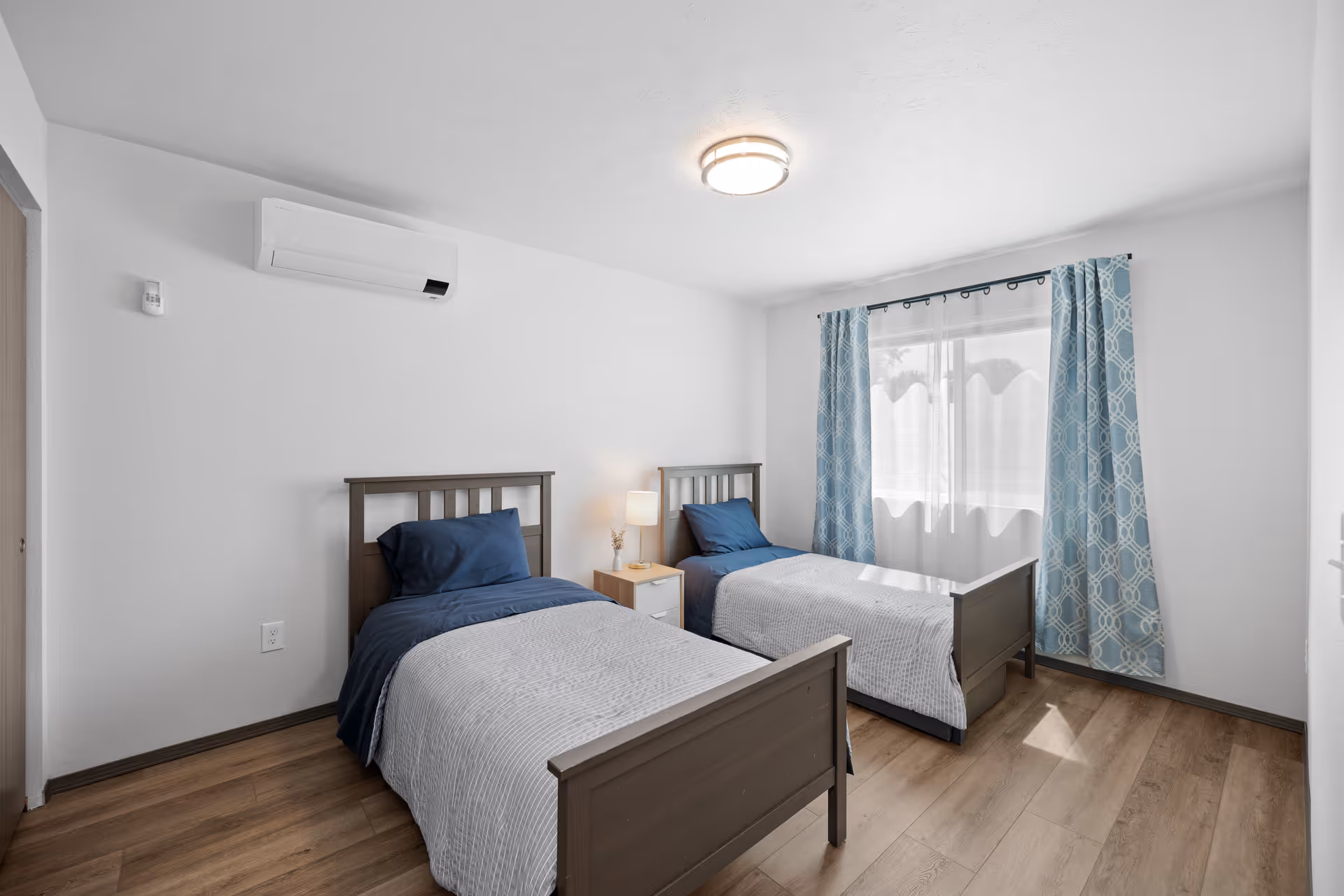 Two single beds with blue bedding in a clean, bright senior living bedroom.