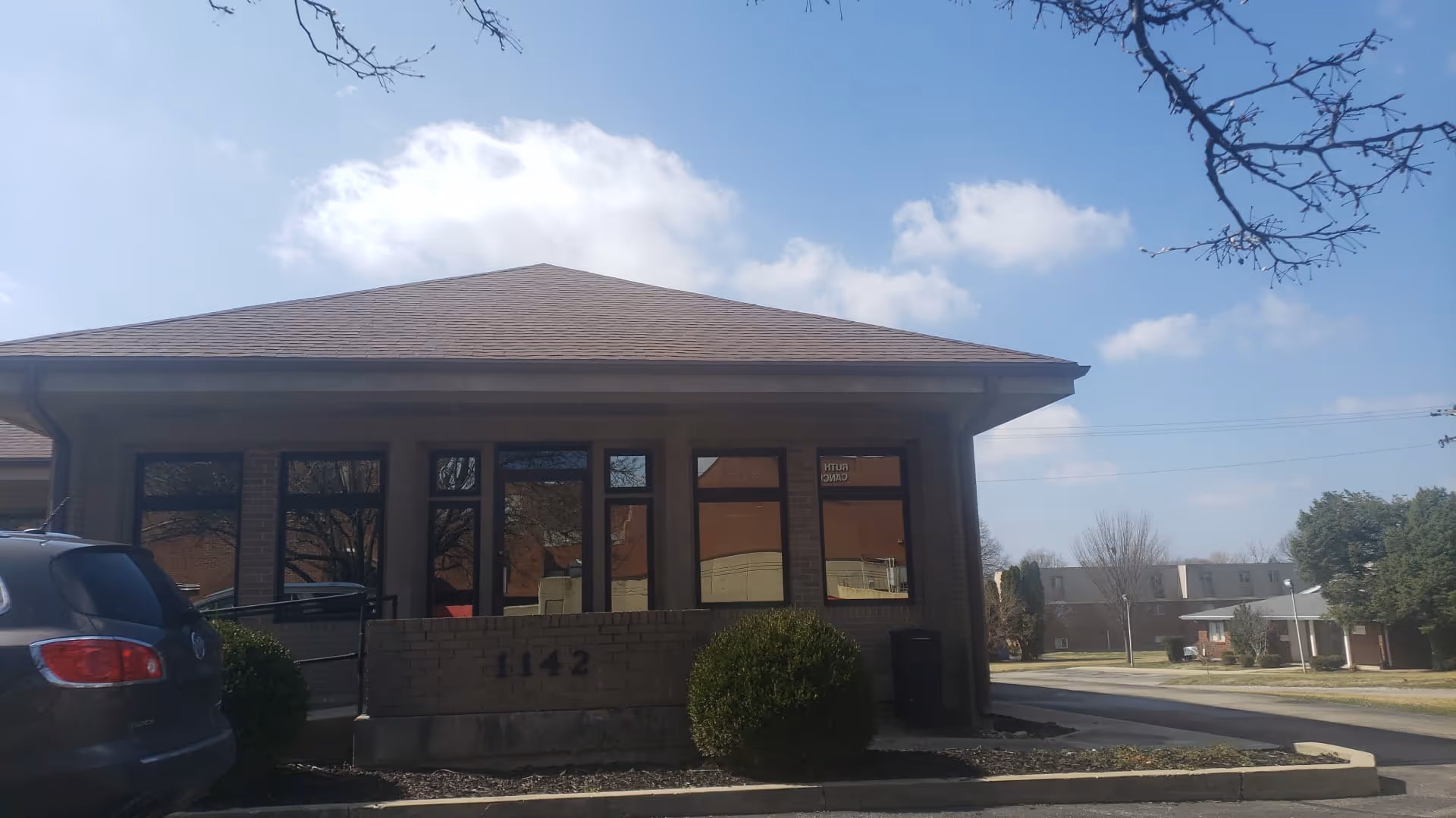 Single story brick facility with large front windows and a low brick barrier at entrance.