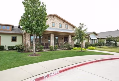 Front view of a stone-faced senior living facility with a covered porch and manicured lawn.