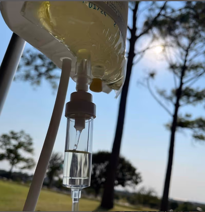 Close-up of an IV drip bag outdoors with trees and sky behind