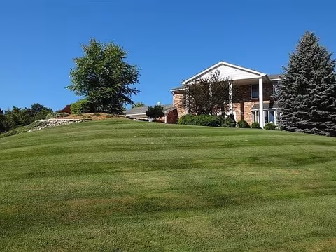 Brick senior living facility with a manicured lawn, trees, and a welcoming entrance.