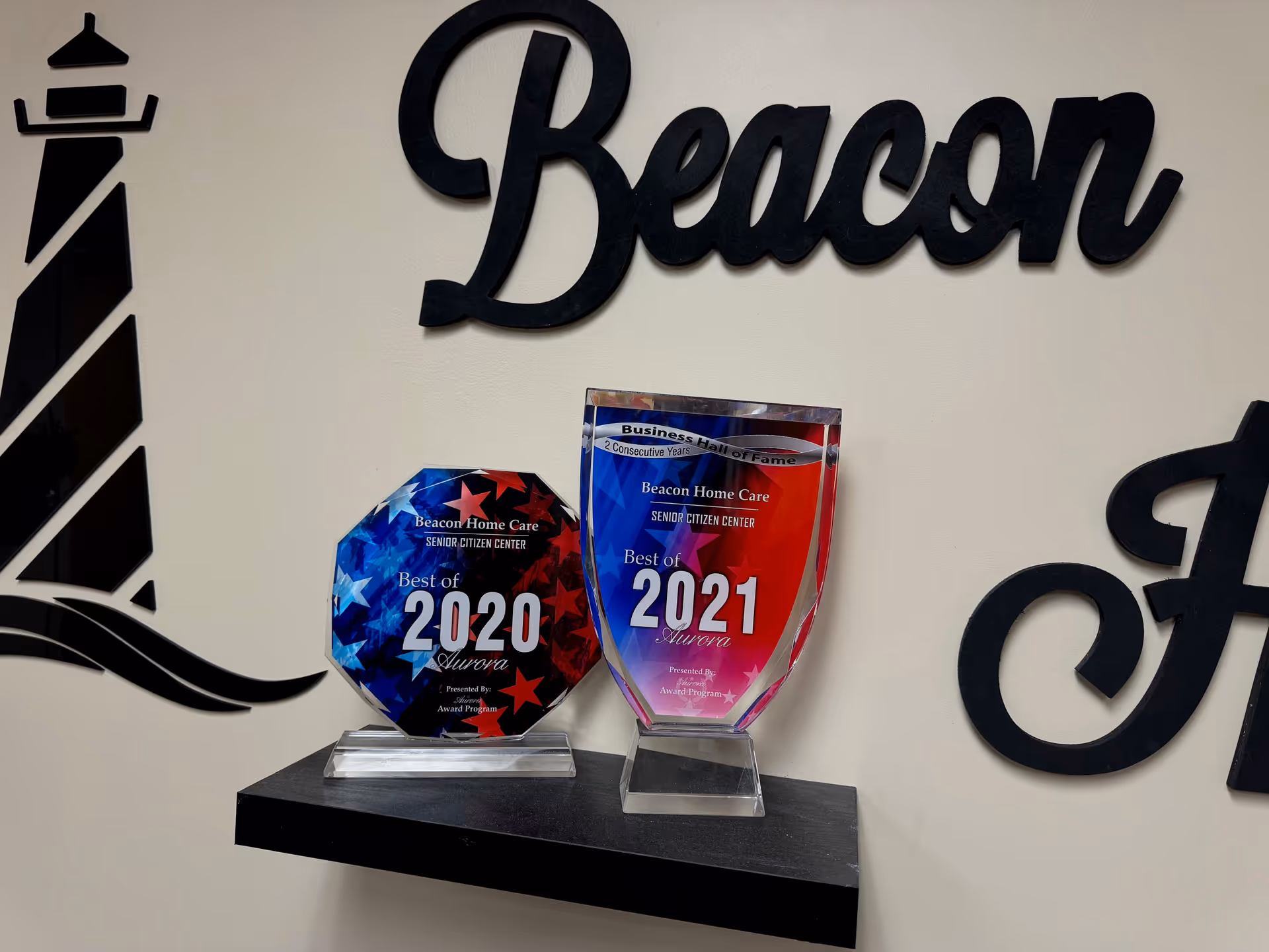 Wall display with Beacon Home Care logo and two award trophies on a shelf.