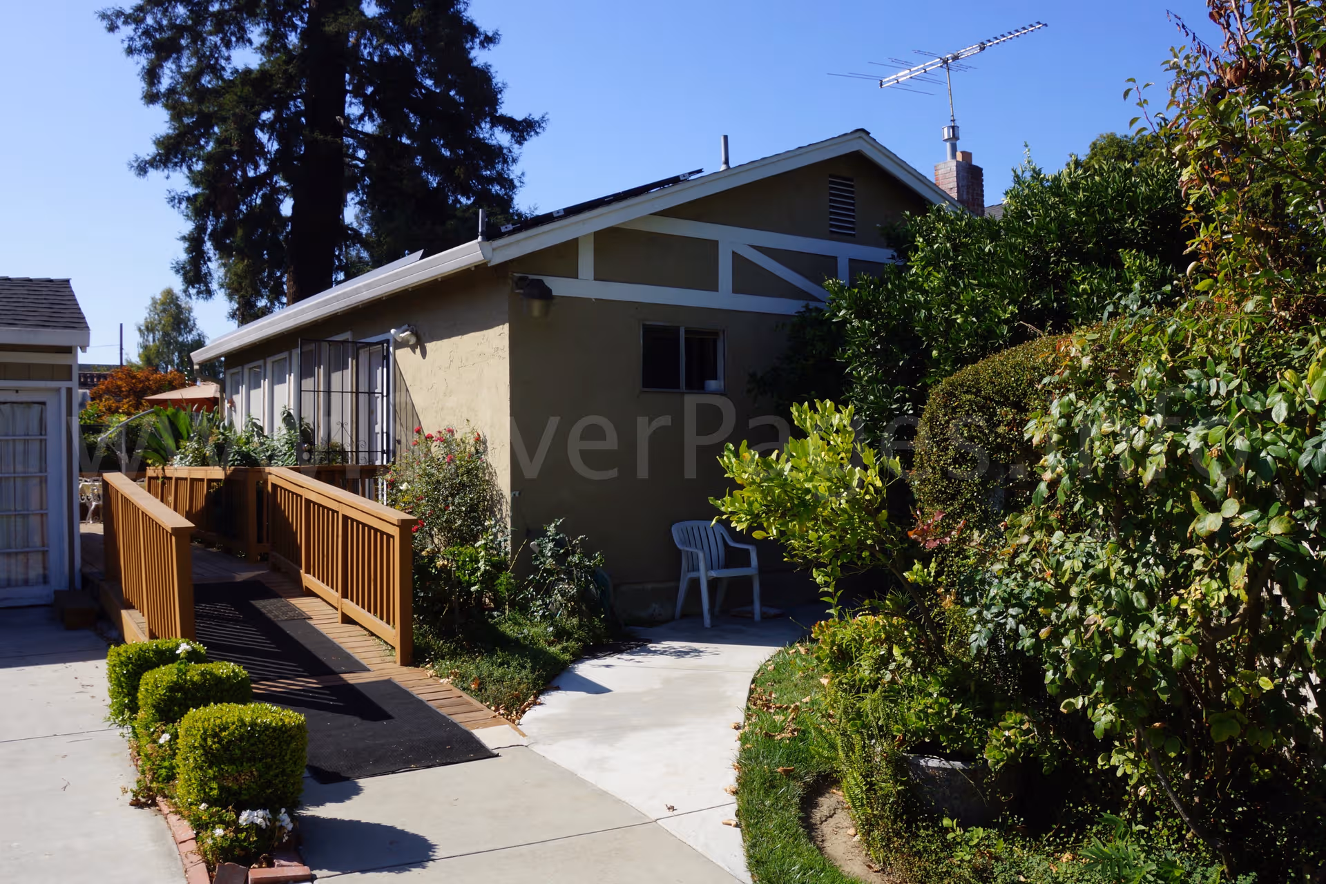 Front exterior of a single-story senior living home with a wooden ramp and garden.