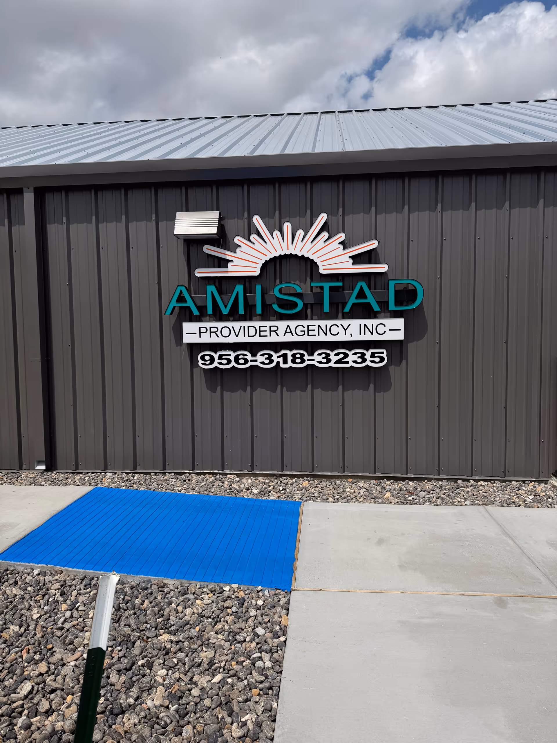 Exterior wall of Amistad Provider Agency sign with sun logo and phone number.