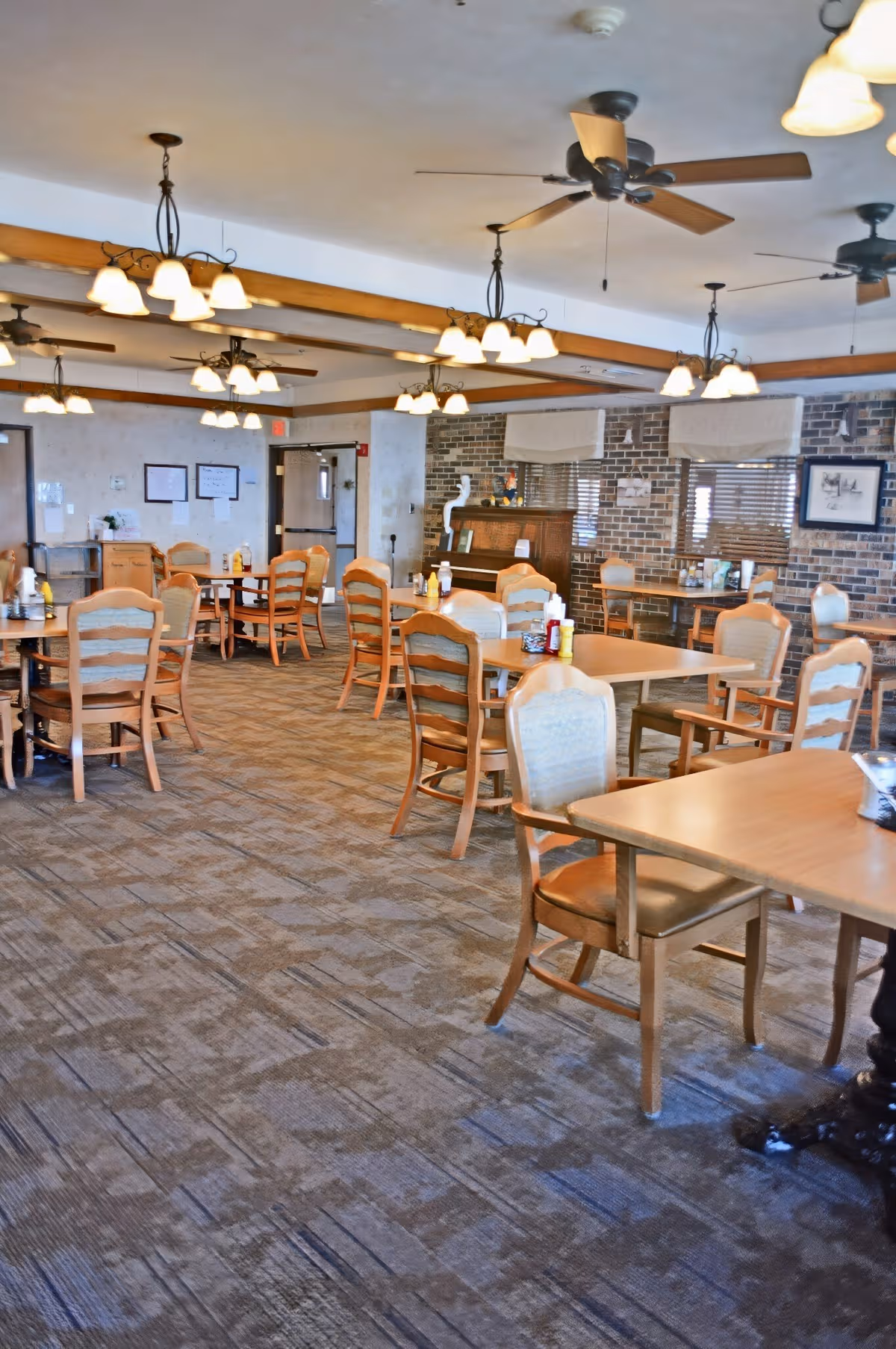 A spacious dining hall with wooden tables, chairs, and ceiling fans.
