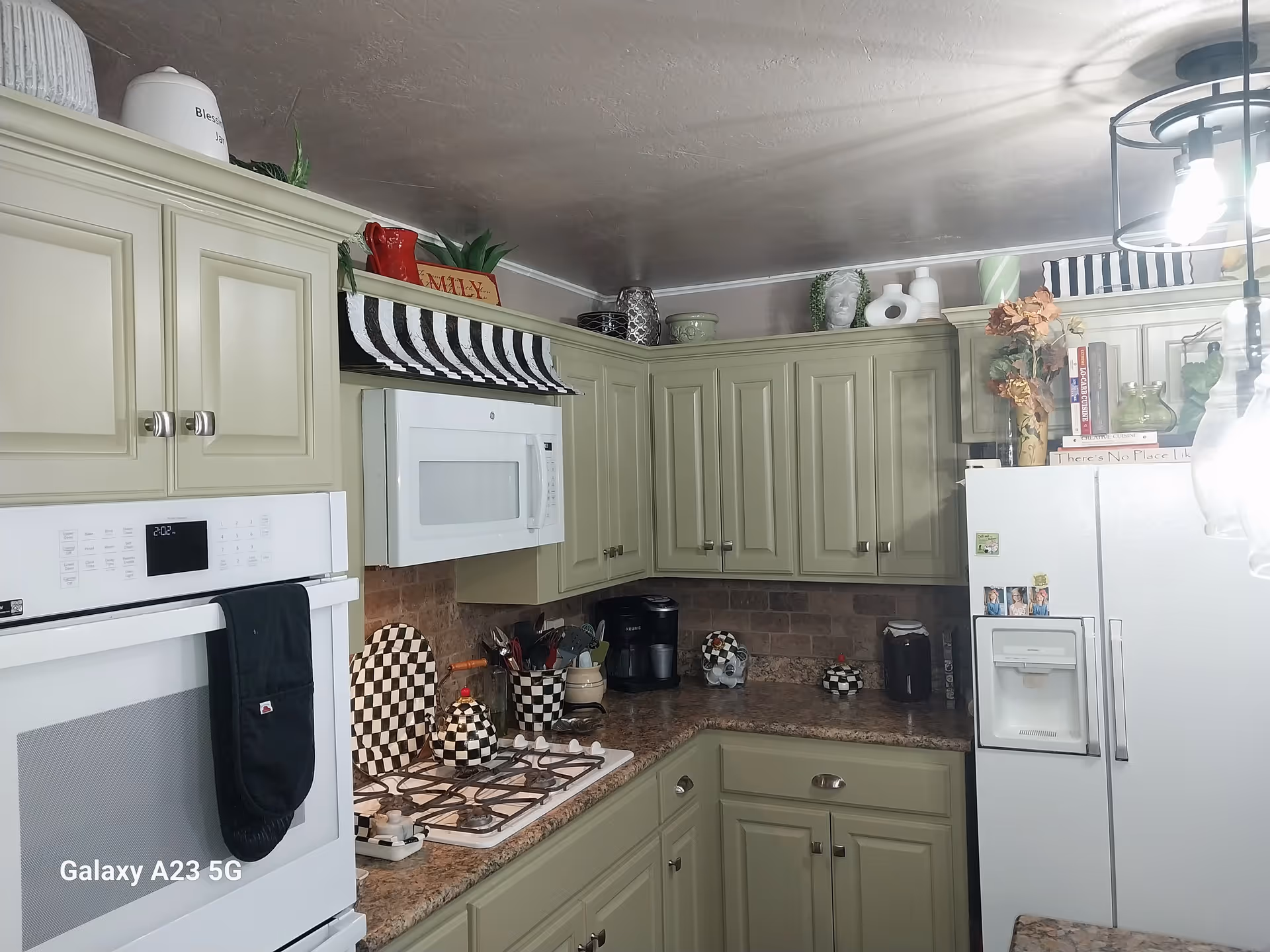 Kitchen with light-green cabinets, white appliances, and checkered decor along granite countertops.