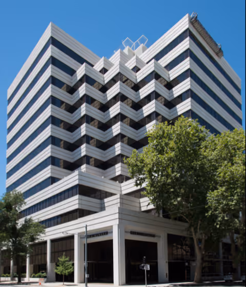 Tall modern building exterior with zigzag balconies and surrounding trees.