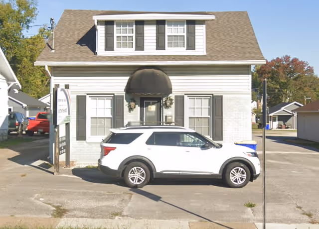 Two-story white building with black awning and parked white SUV in front.