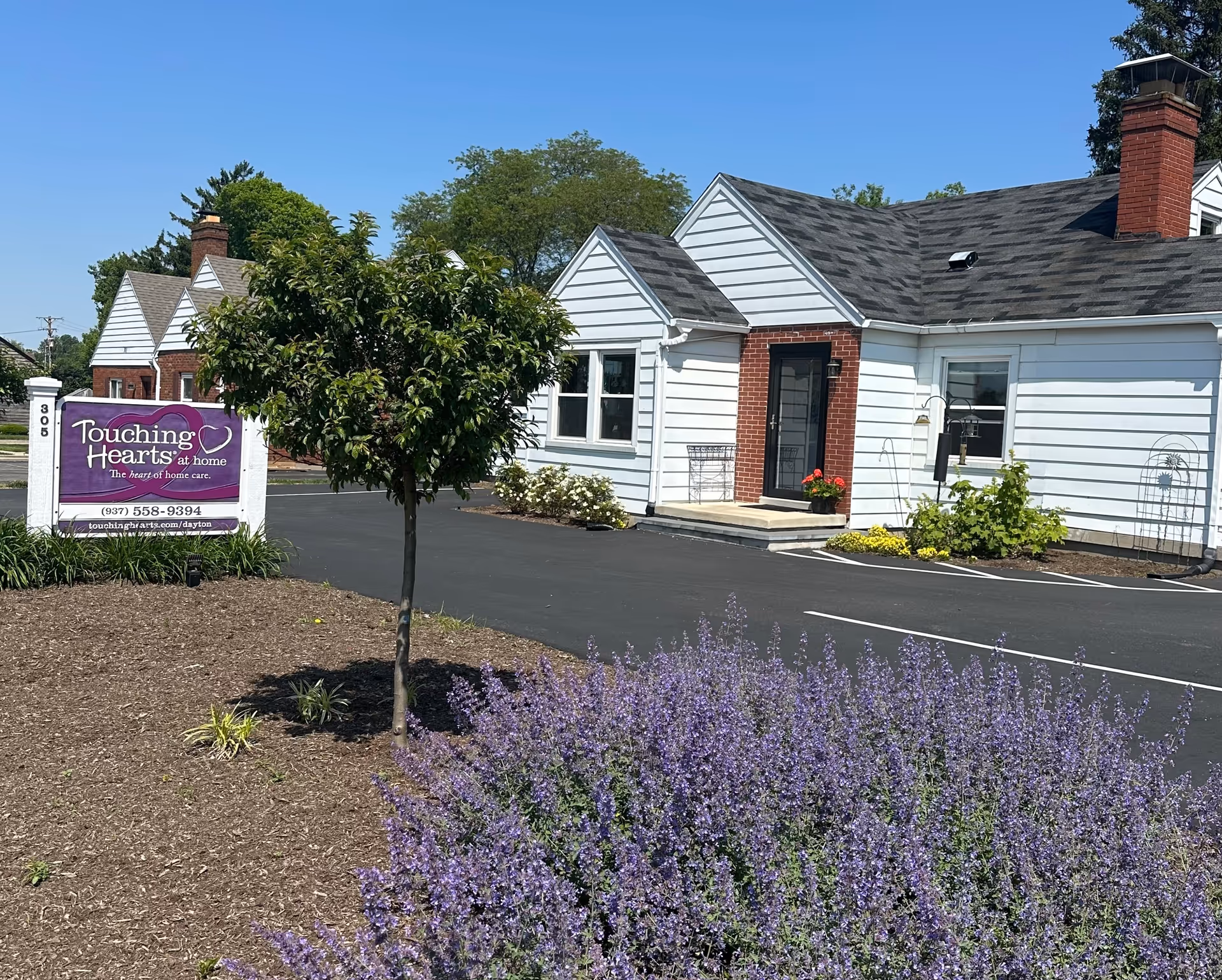 Single-story senior living facility exterior with a purple Touching Hearts sign and landscaped frontage.