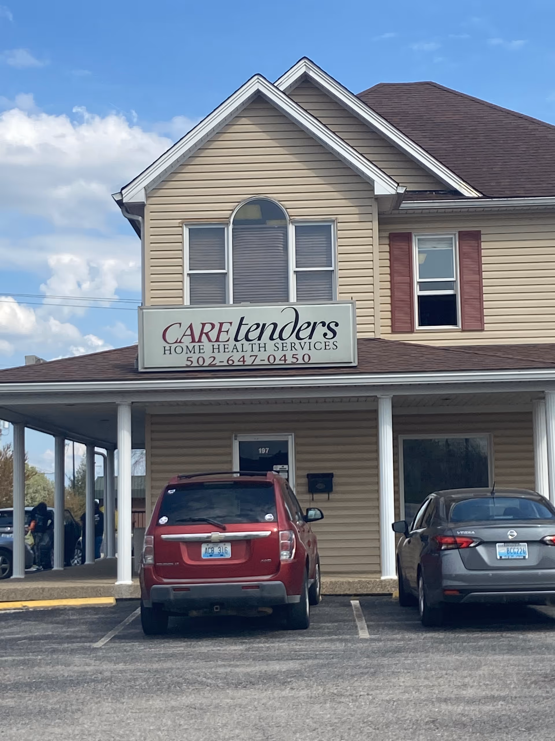 Two-story beige building with Caretenders sign, covered entrance, and parked cars.
