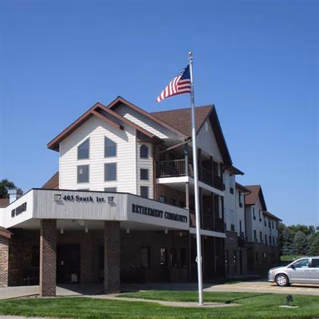 Exterior view of a retirement community building with balconies and an American flag.