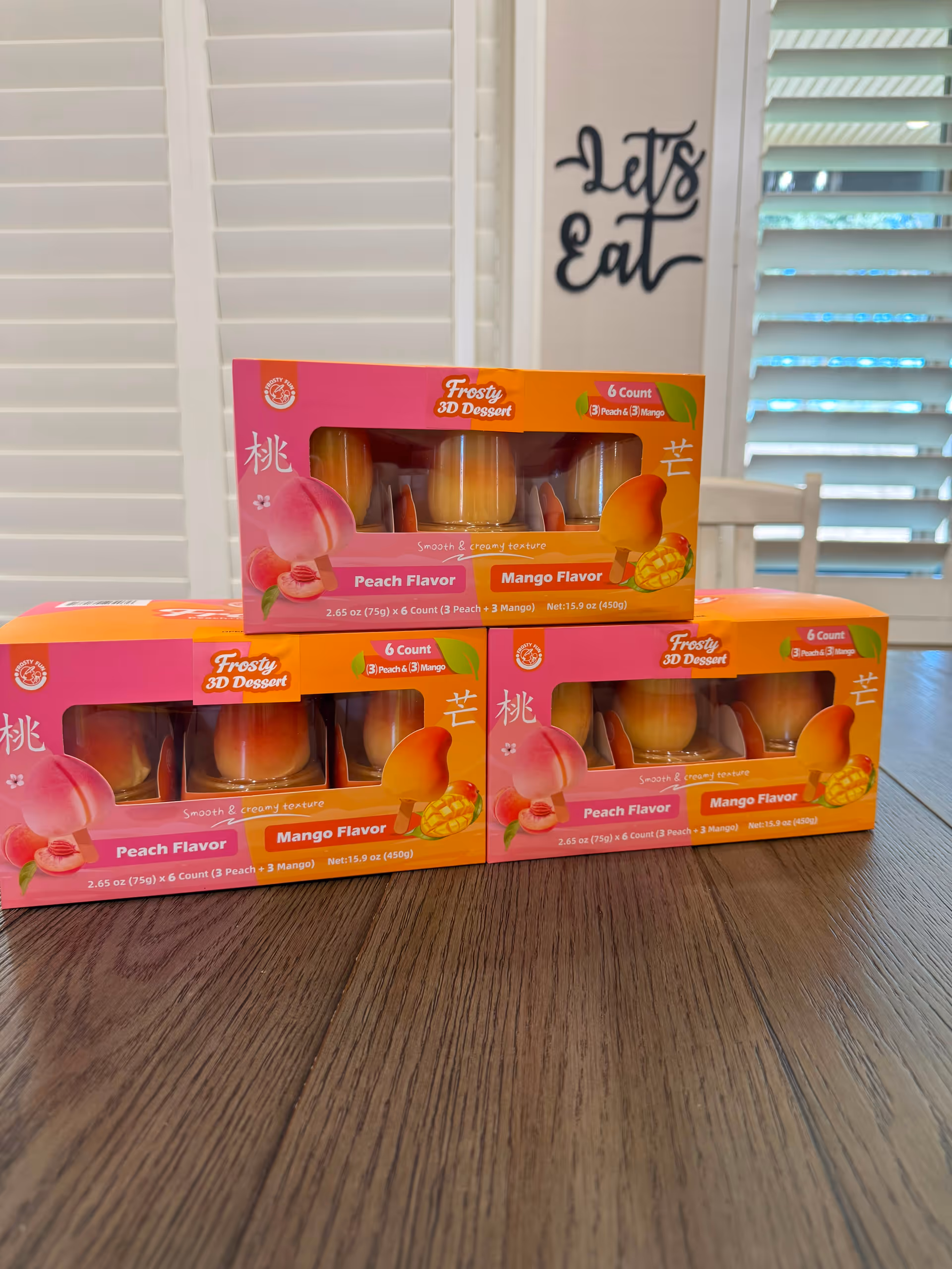 Boxes of Peach and Mango Frosty 3D Dessert sit on a wooden dining table indoors.