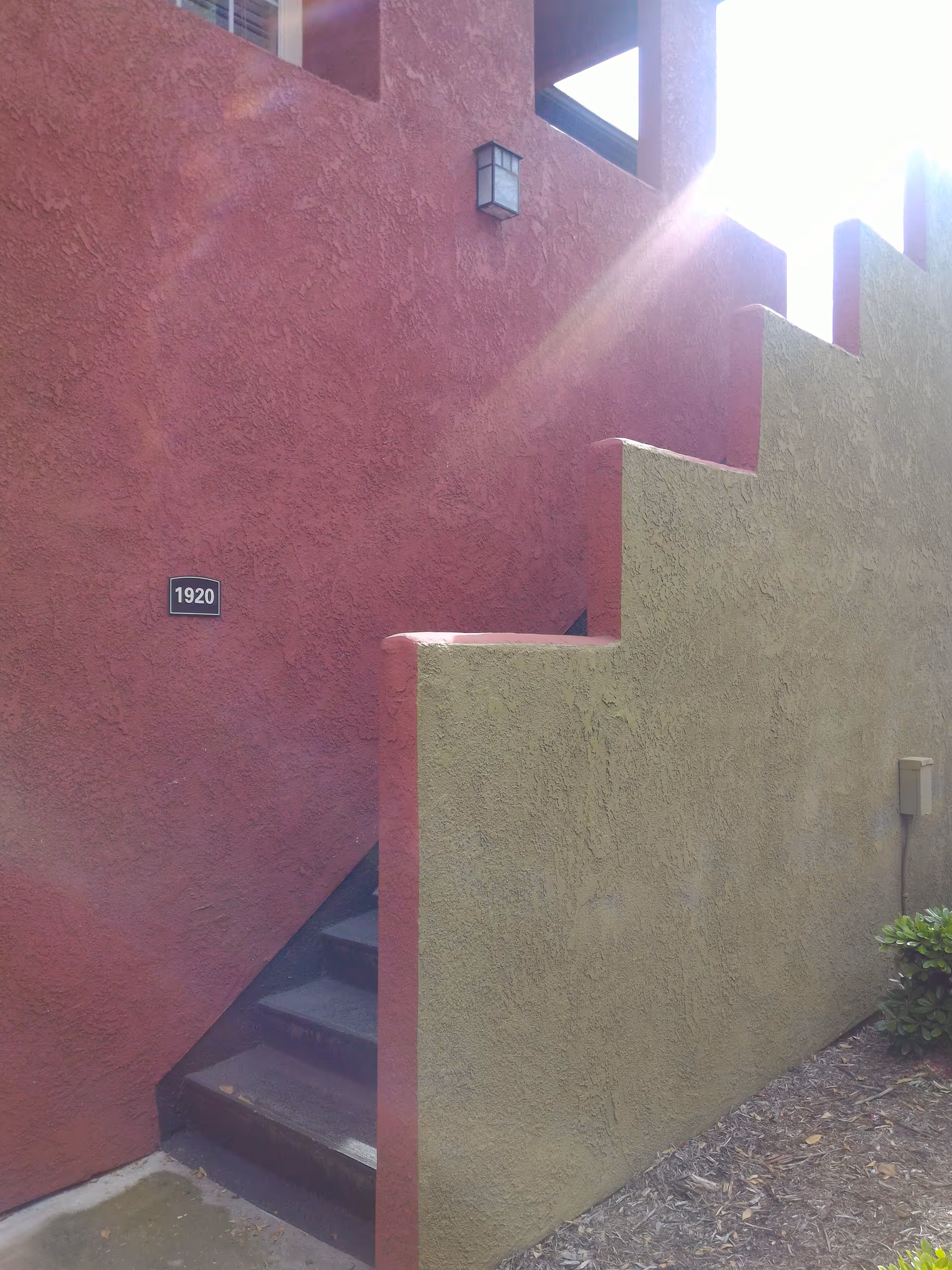 Colorful stucco exterior with red and tan walls, stairs, and sun glare.