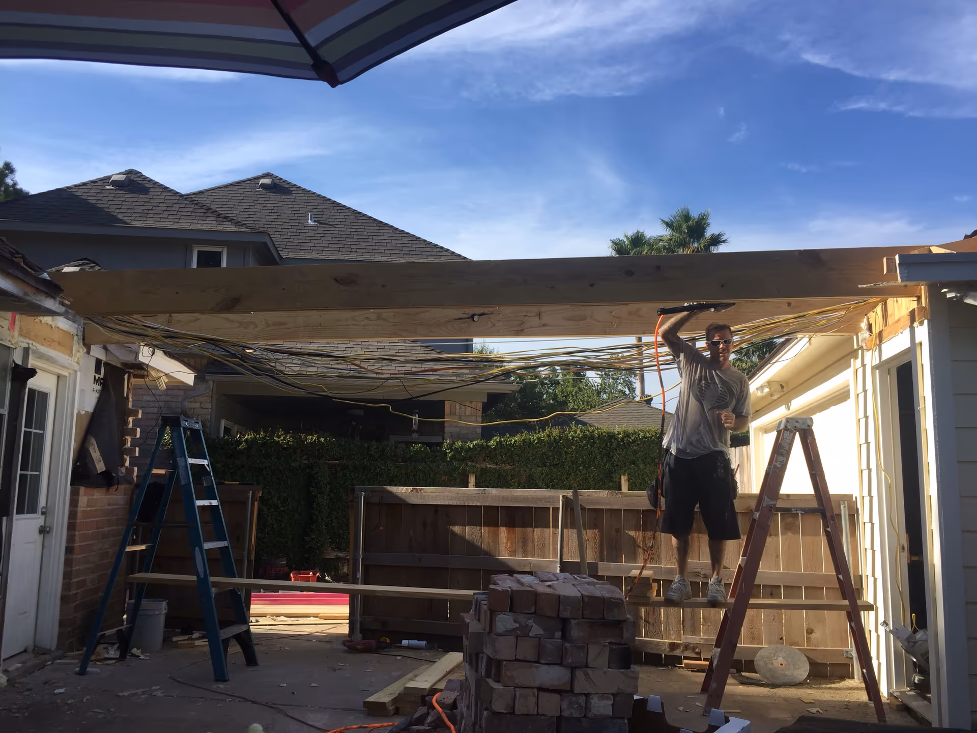Worker on ladder raises a wooden beam in a backyard construction site.