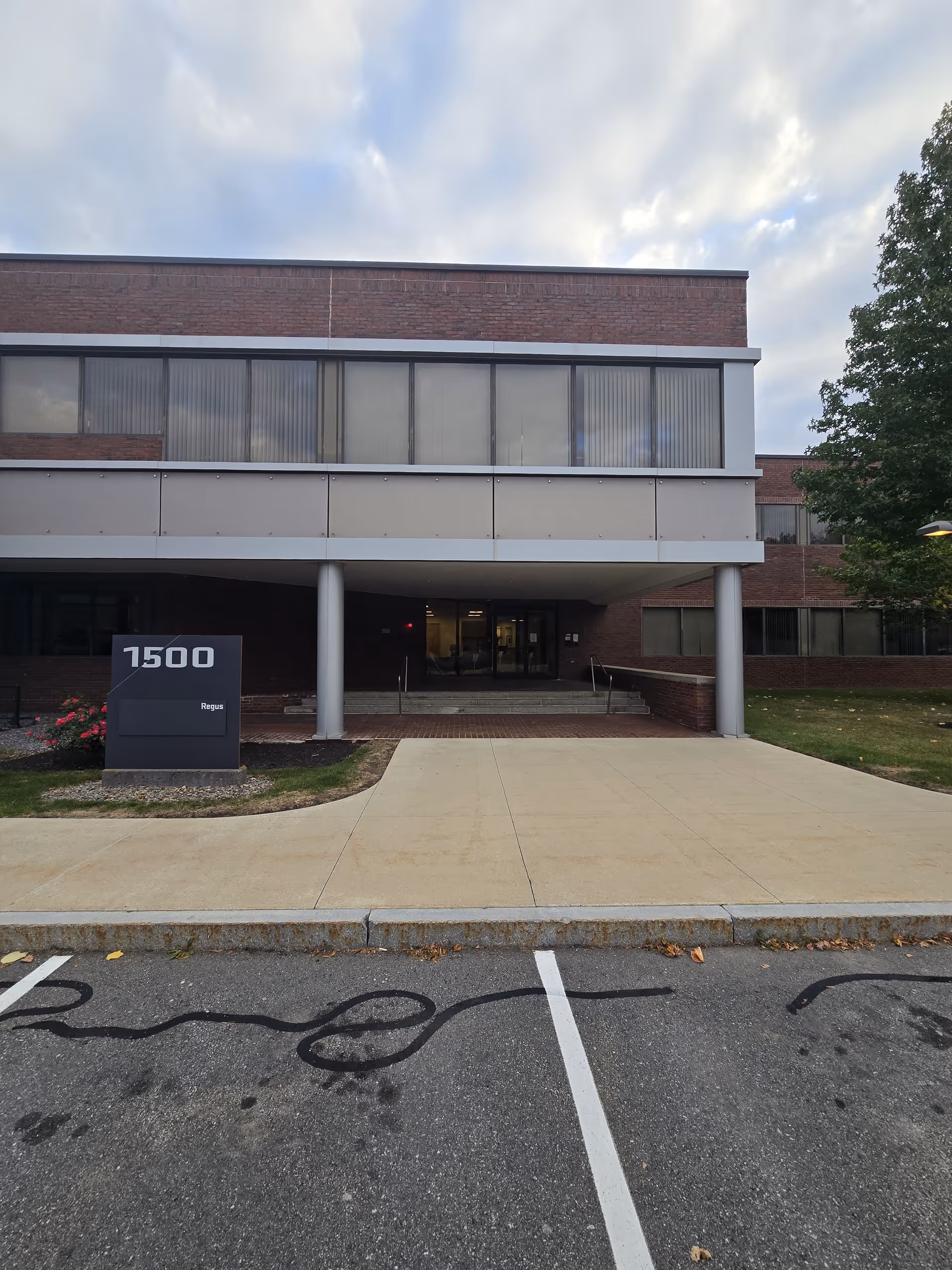 Front view of a brick building entrance with a sign and empty parking lot.