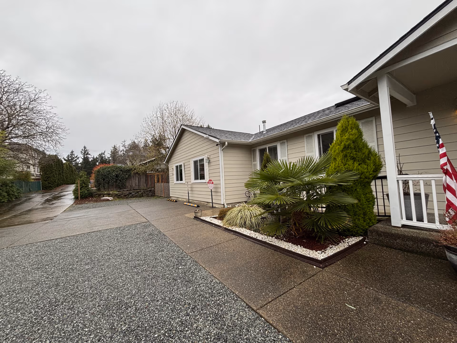 Single-story beige senior living facility exterior with driveway, landscaping, and American flag at entrance.