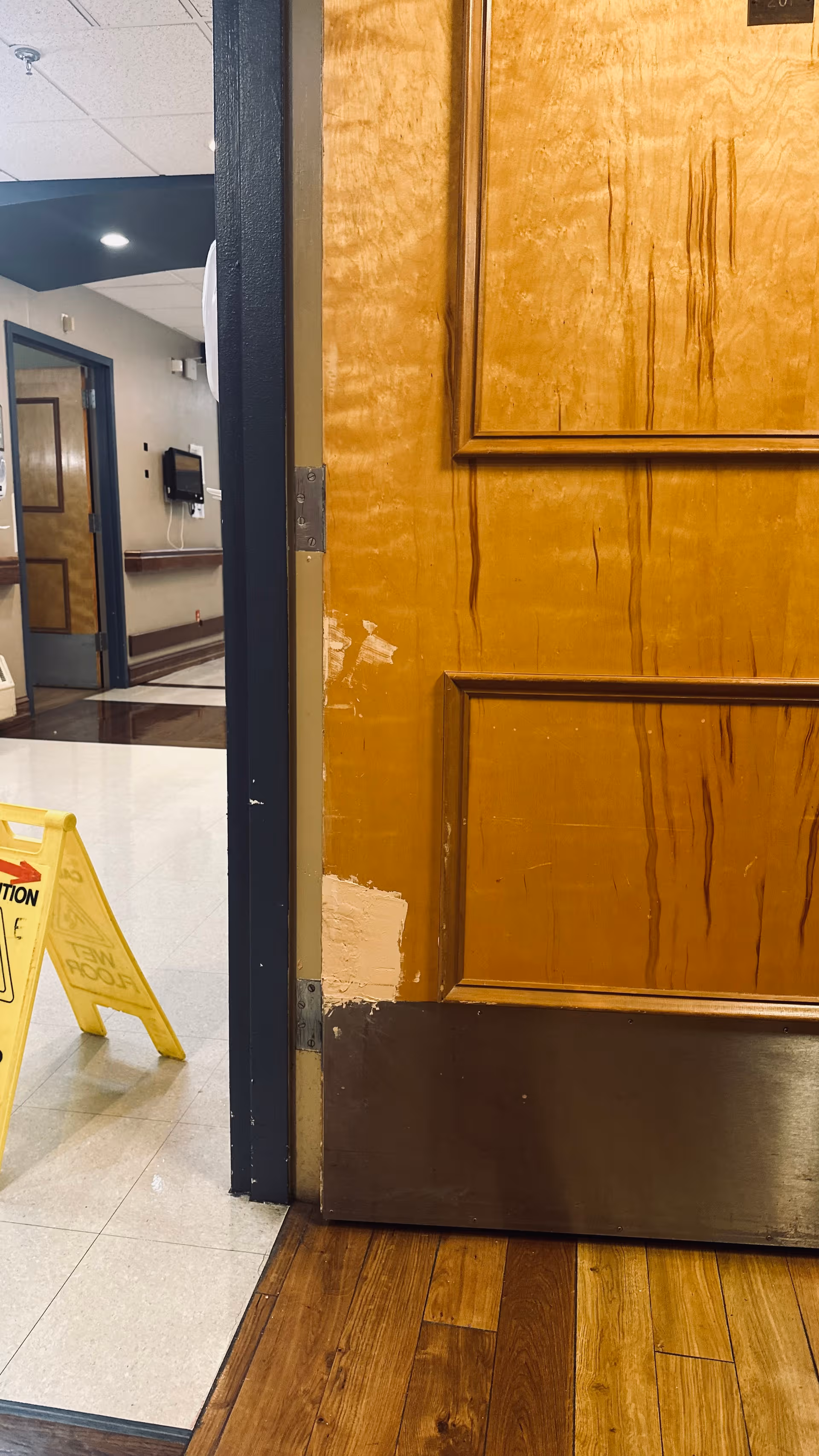 Open wooden door with wear leads into a hallway inside Webster Park Rehabilitation & Healthcare Center.