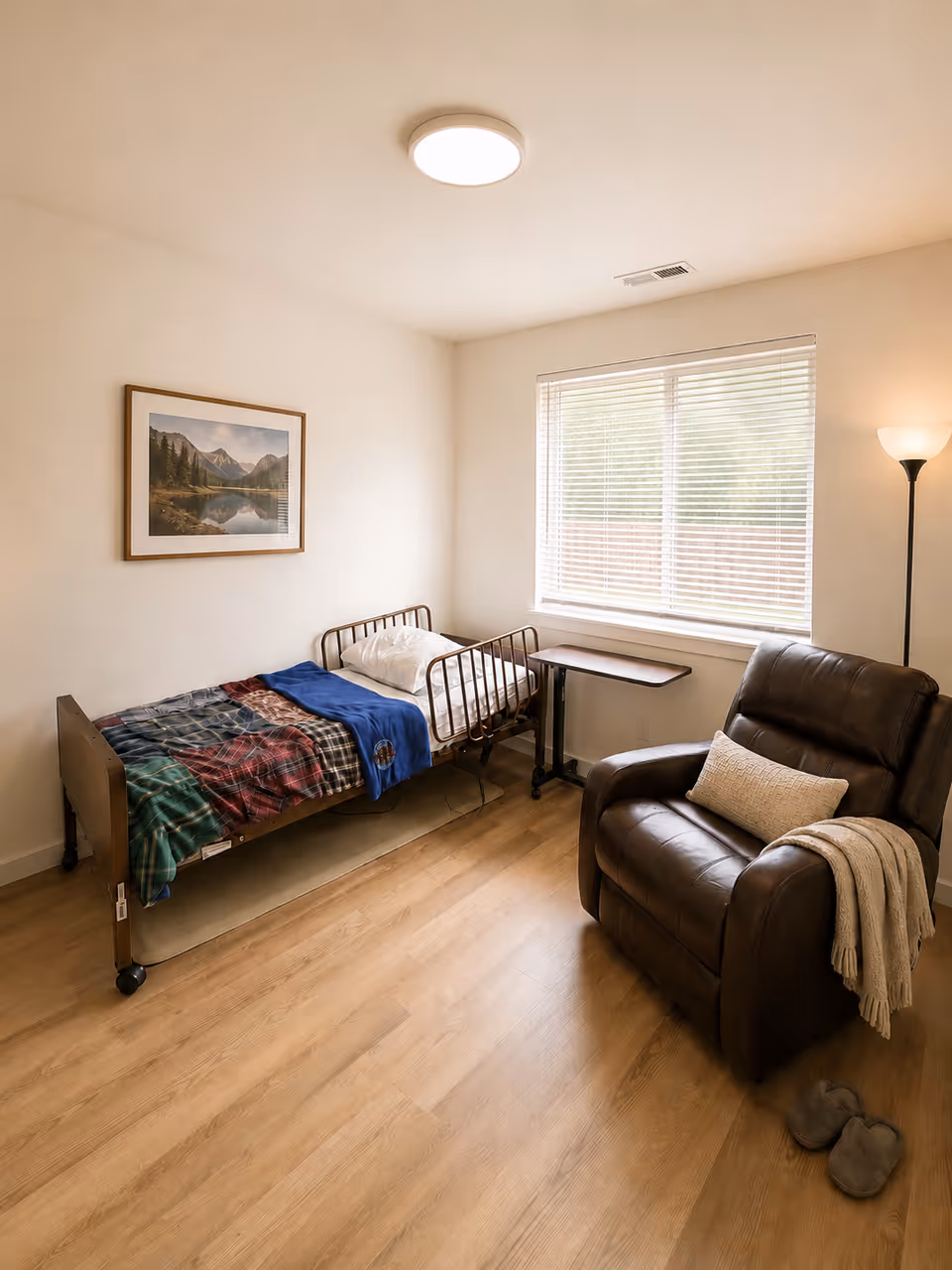 A small bedroom in a senior facility with a single bed, plaid blanket, and recliner.