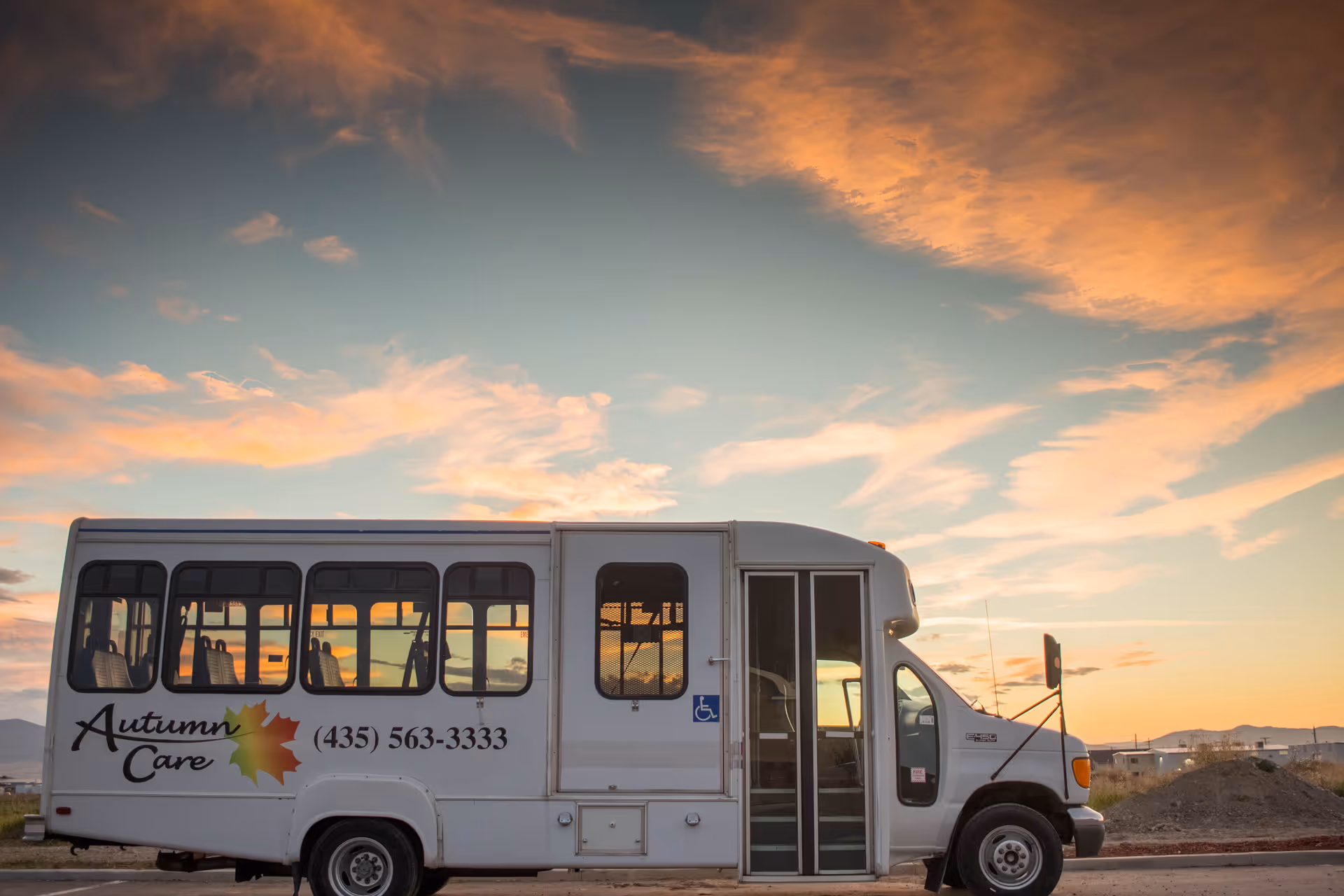 White Autumn Care bus parked outdoors at sunset with logo and phone number.