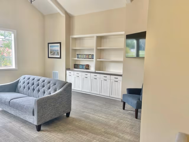 Bright lounge area with a gray tufted sofa, built-in shelves, and a wall-mounted TV.