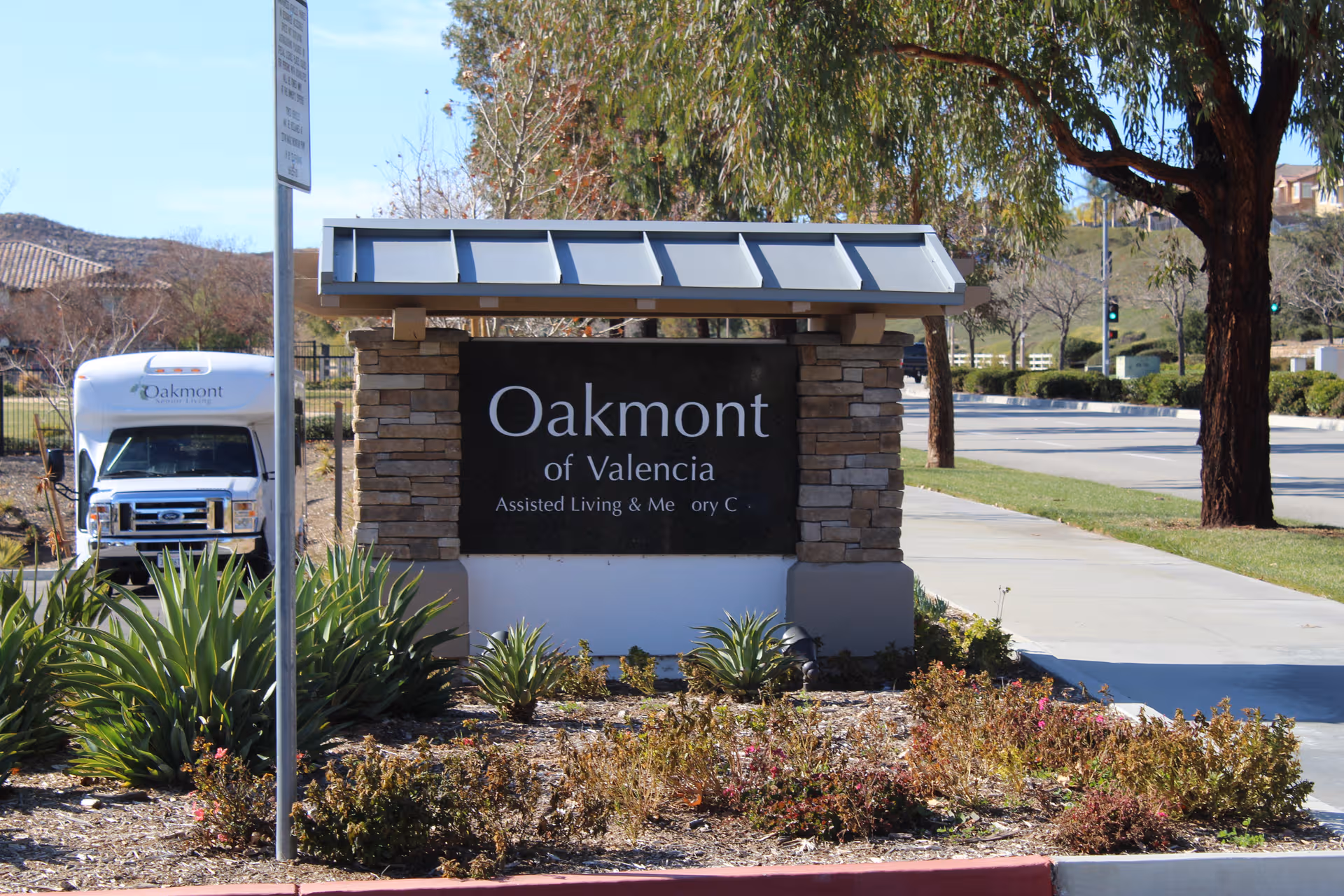 Oakmont of Valencia entrance sign with stone structure, surrounding landscaping, and nearby street.