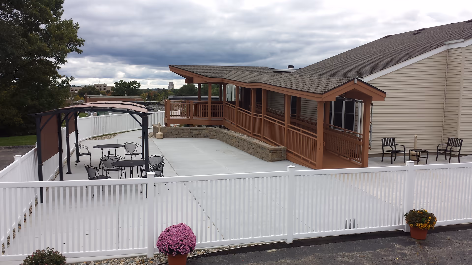 Outdoor patio area with white fence, seating, and a wooden porch attached to the building.