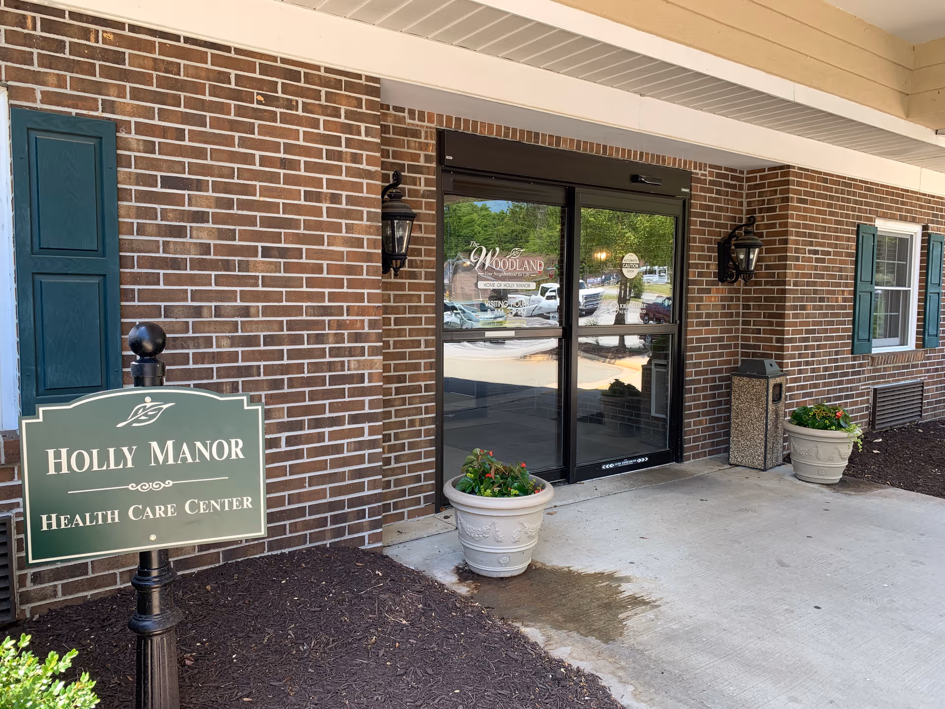 Brick exterior entrance of a senior living facility with glass doors and planters.