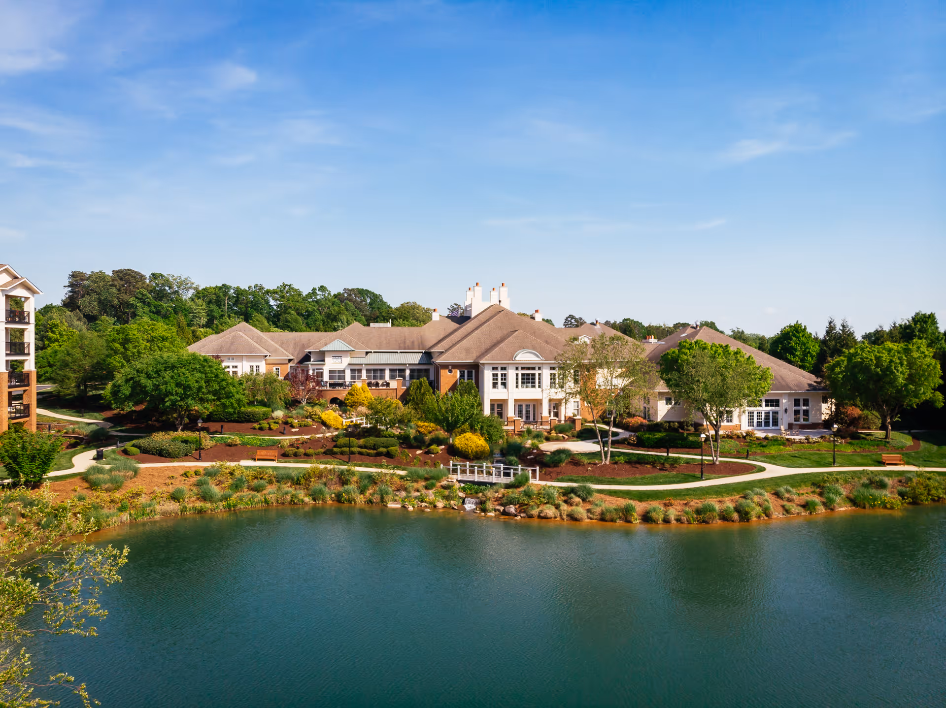 A large senior living campus sits along a lake with manicured grounds and a central building.