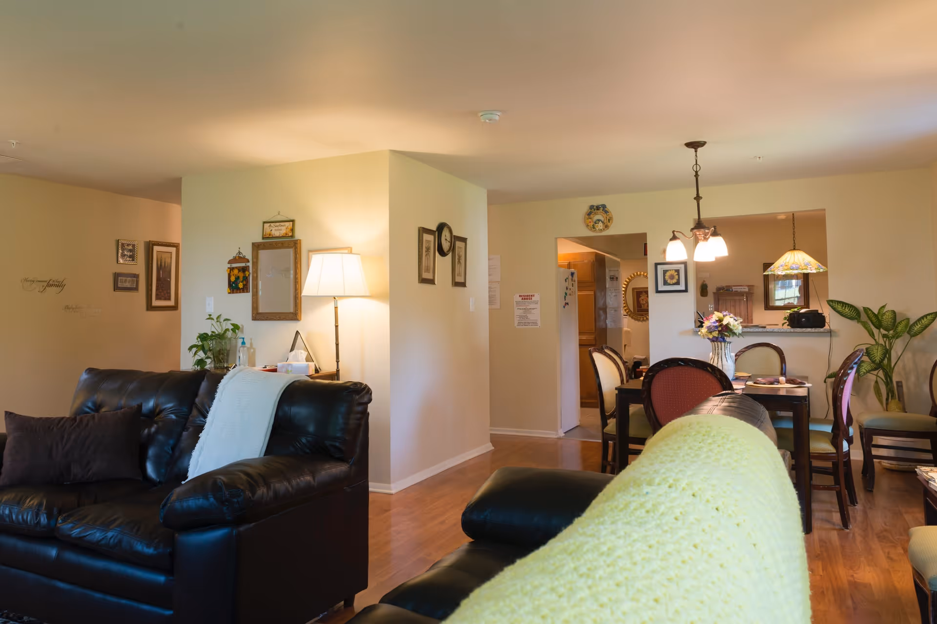 Open living room and dining area with leather sofas, a floor lamp, and a dining table under pendant lights.