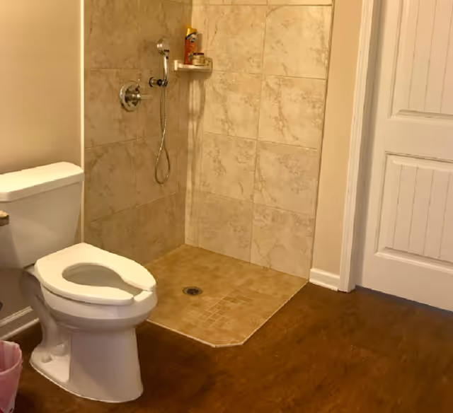 Small bathroom with a toilet and tiled shower area, door on the right.