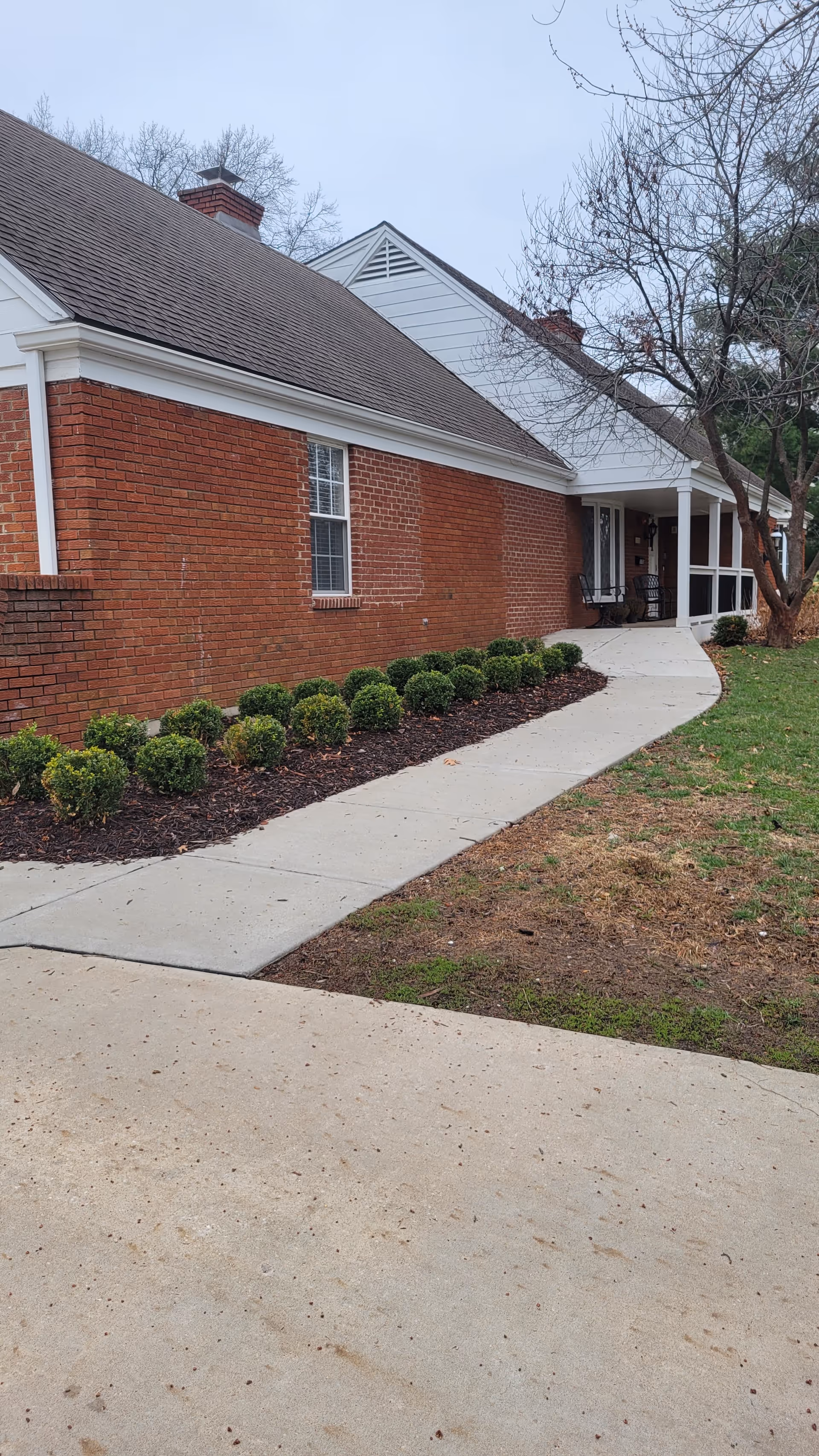 Brick senior living facility exterior with curved walkway and shrub landscaping.