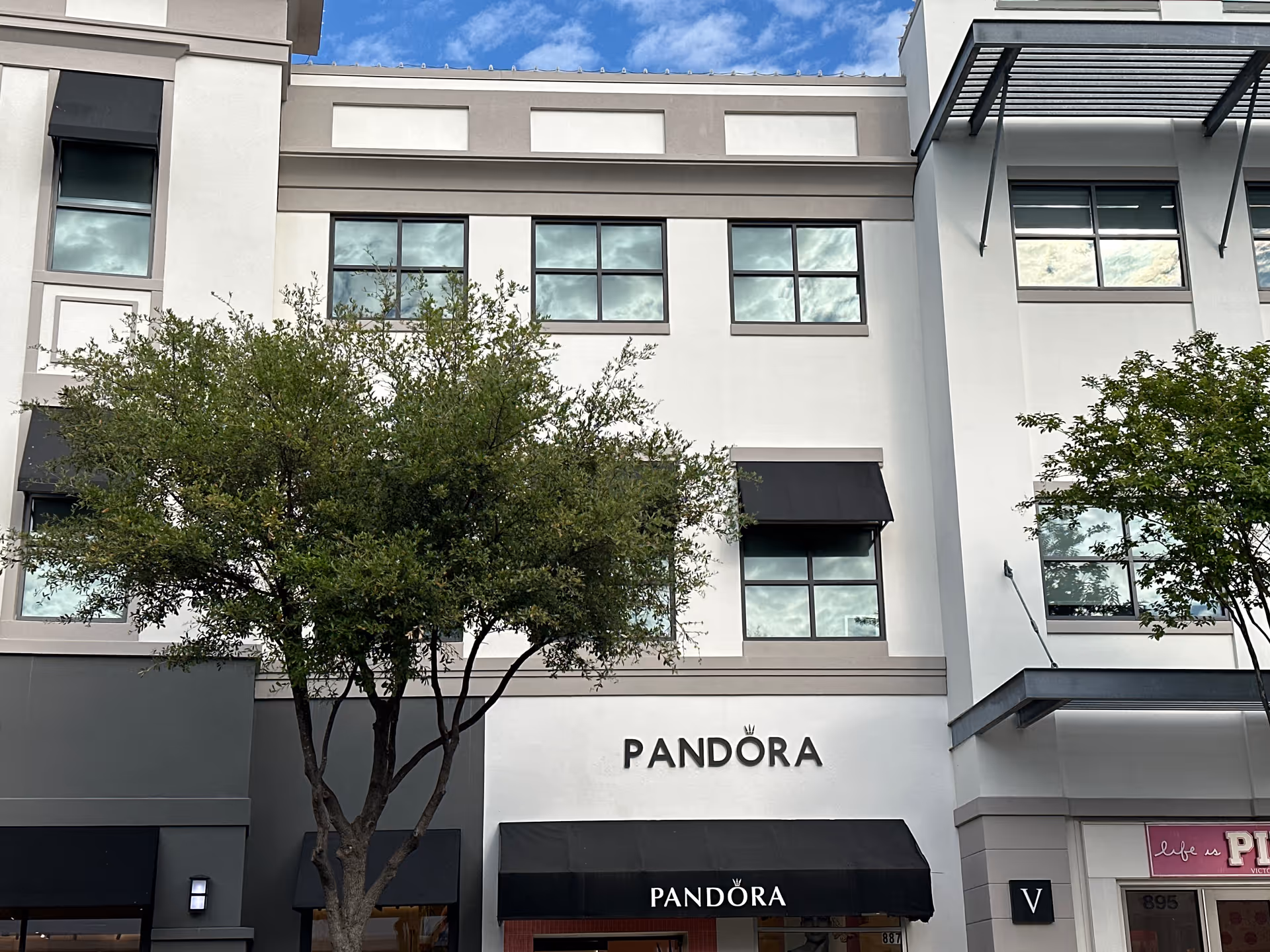Facade of a modern shopping building with Pandora storefront and trees.