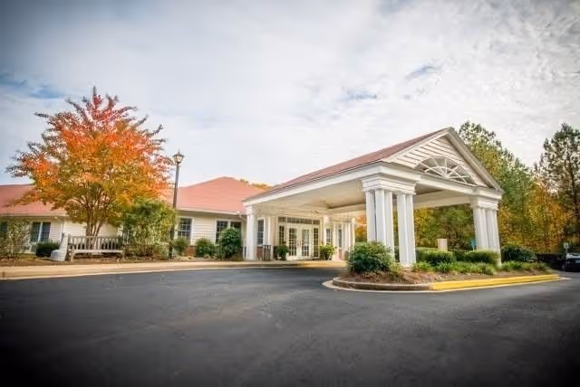 Exterior view of a senior living center with a covered entrance and autumn trees.
