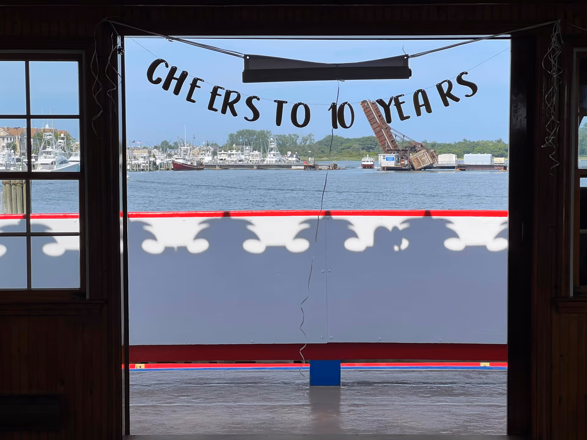 Interior doorway frames a waterfront view featuring a 'Cheers to 10 Years' banner.