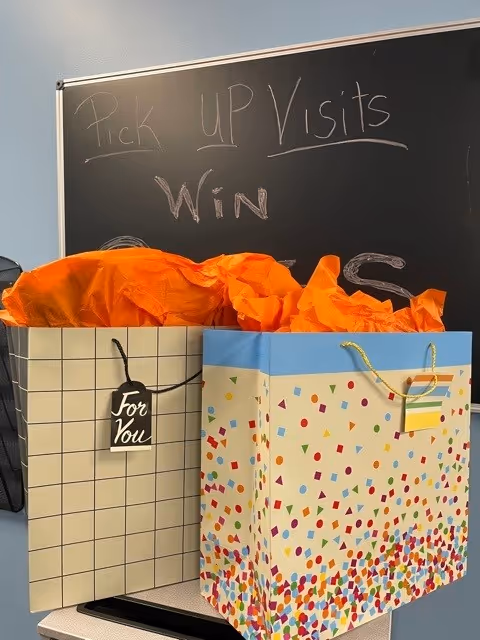 Two decorative gift bags with orange tissue sit in front of a chalkboard.
