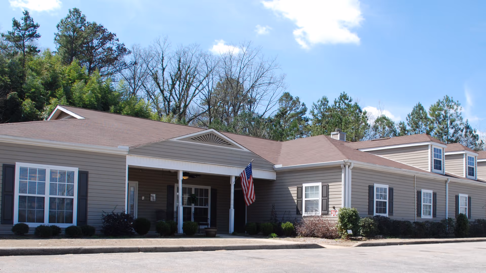 Exterior view of Gardens of Pelham, a single-story senior living facility with front entrance and flag.