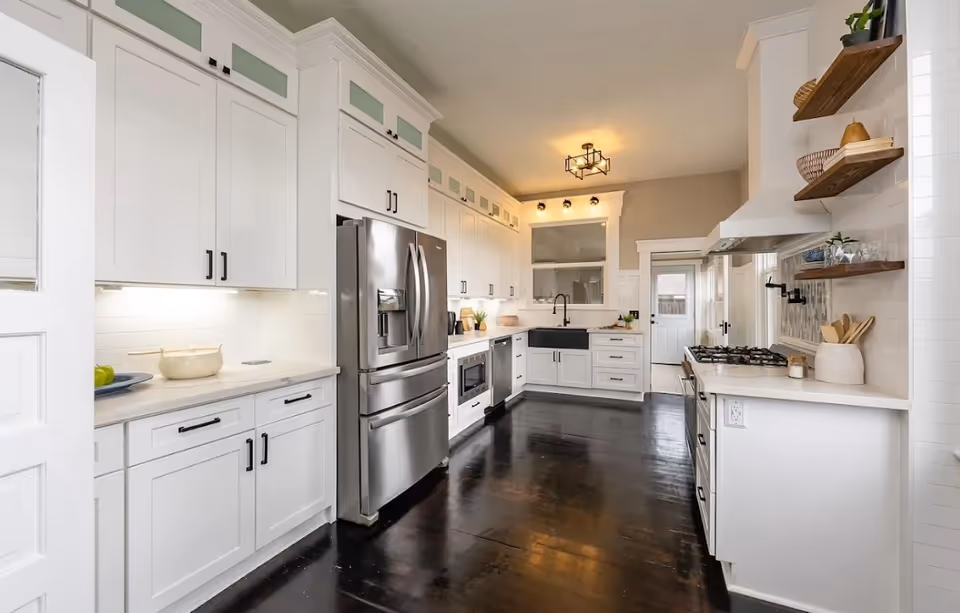 Bright white kitchen with stainless steel appliances, dark wood floor, and open shelving.