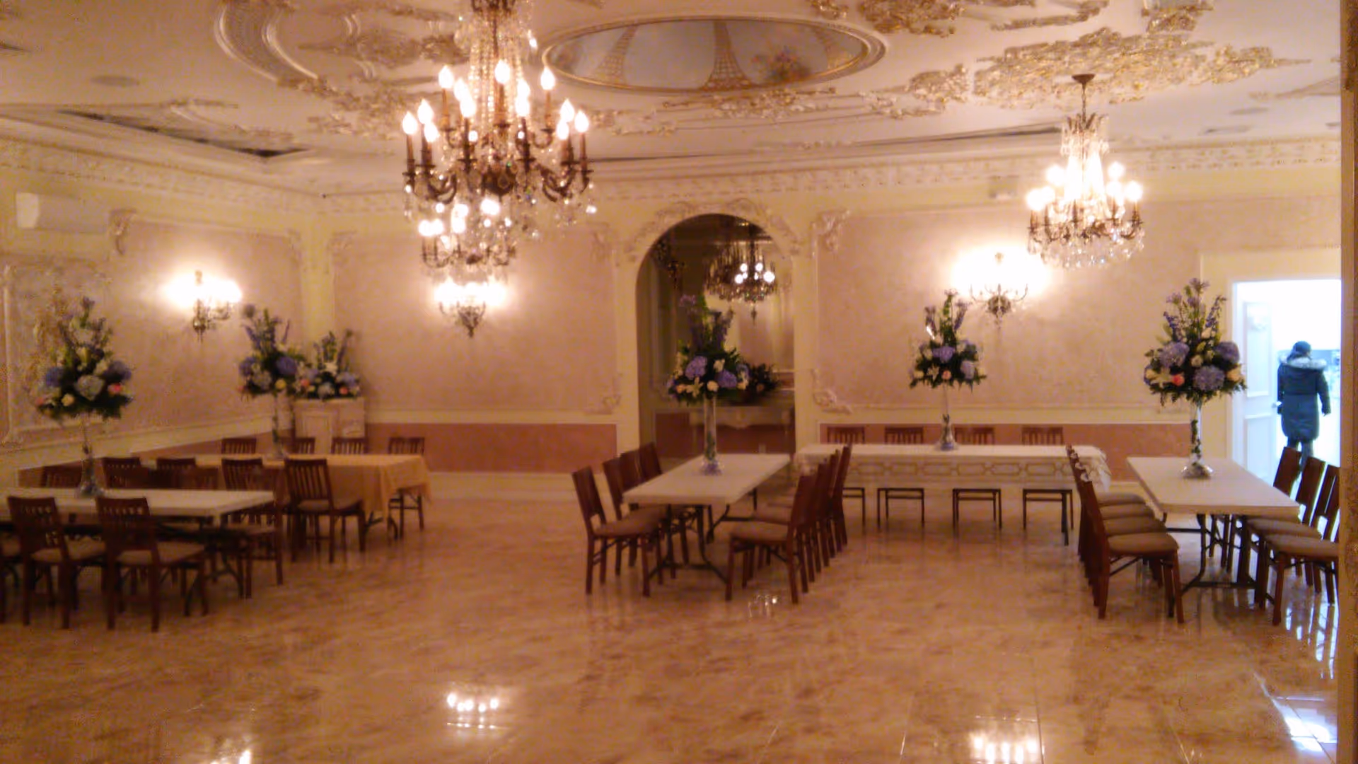 Elegant banquet hall interior with chandeliers, long dining tables, chairs, and floral centerpieces.