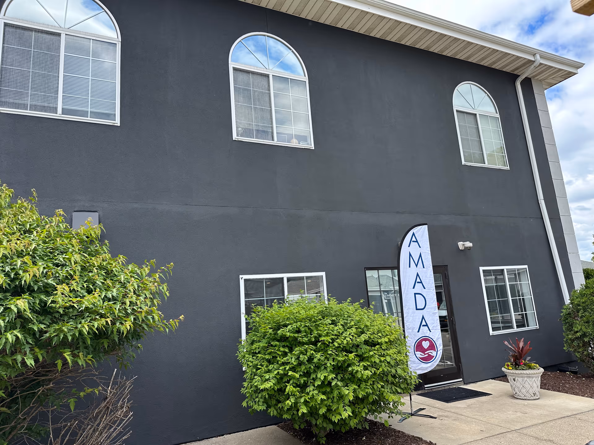 Dark gray two-story building with arched windows and an Amada Senior Care banner at the entrance.