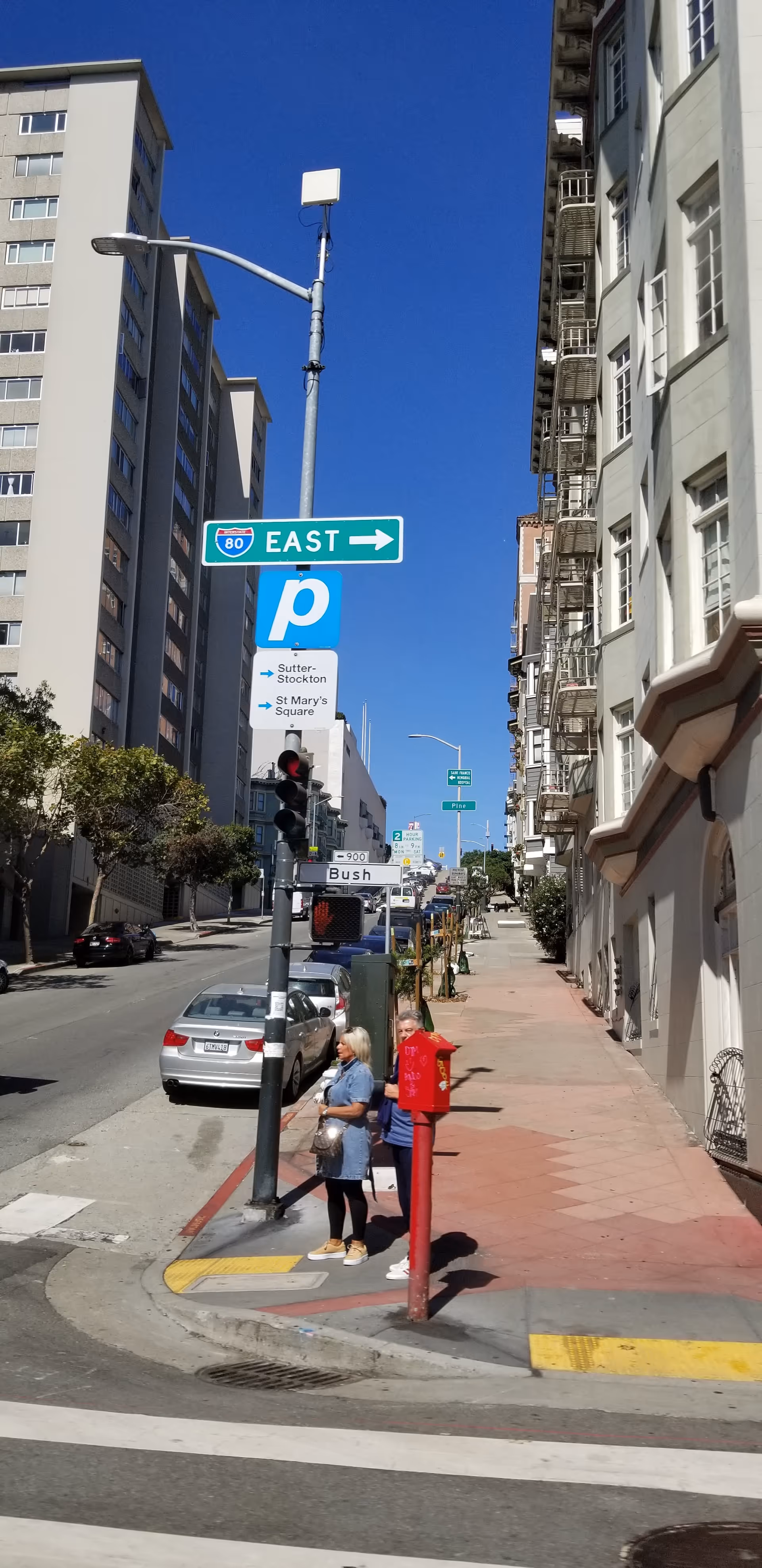 Urban city street with tall buildings, pedestrians, cars, and street signs.