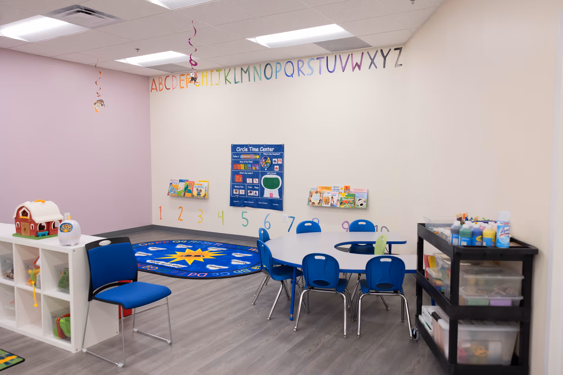 Bright children's activity room with alphabet wall, rug, tables, and toy shelves.