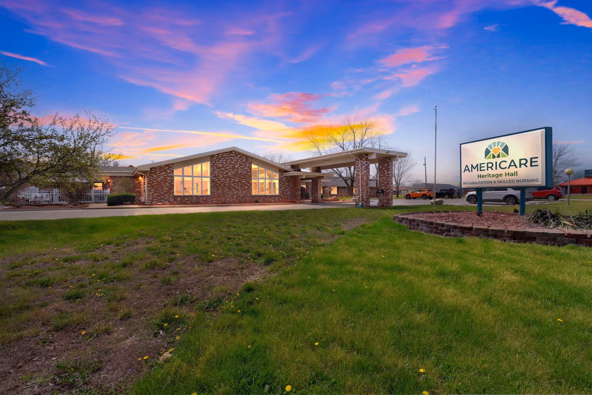 Sunset over Heritage Hall senior living facility with brick exterior, entrance canopy, and sign.