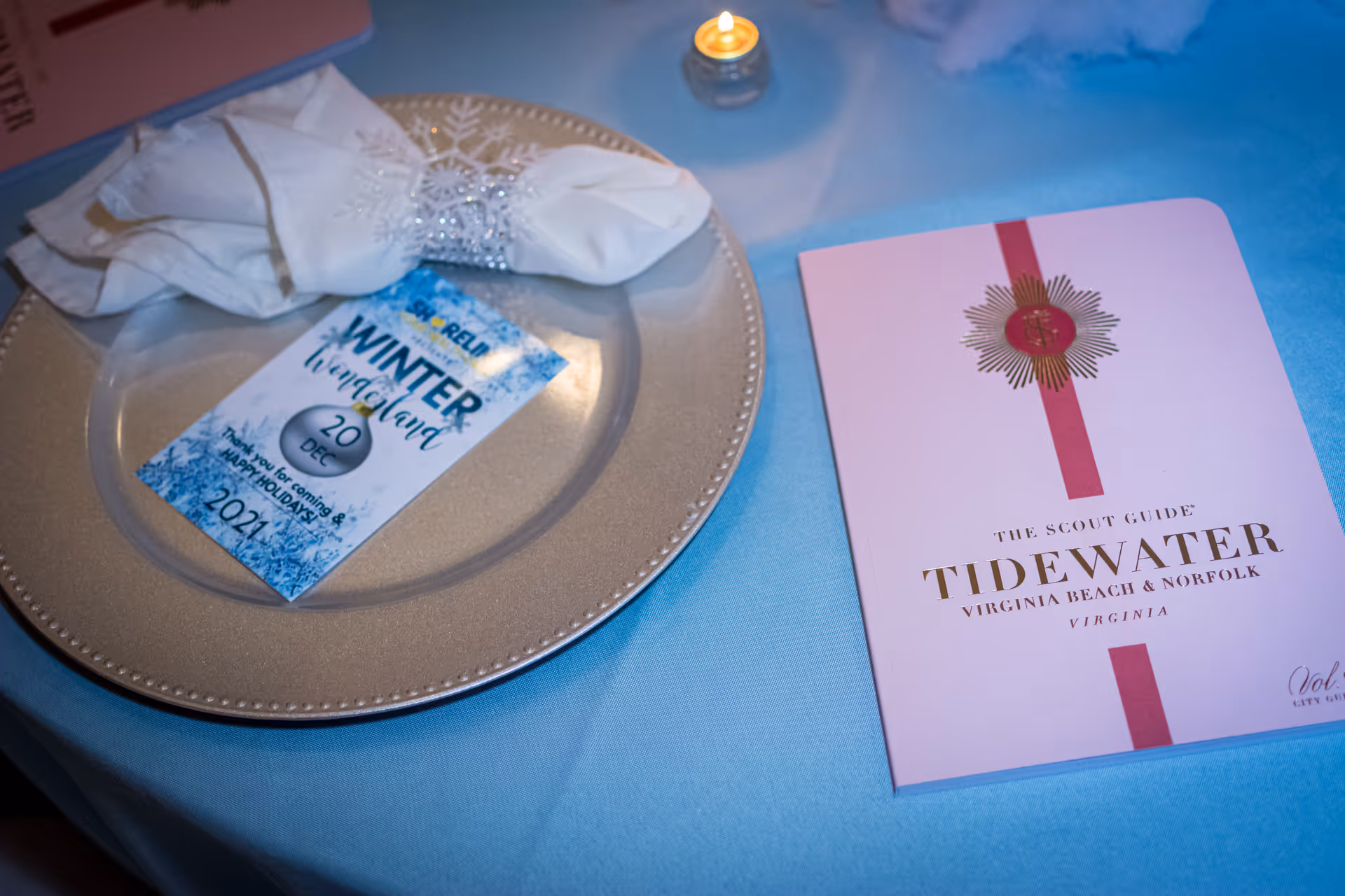Table setting with plate, napkin, and event brochure on a blue tablecloth.