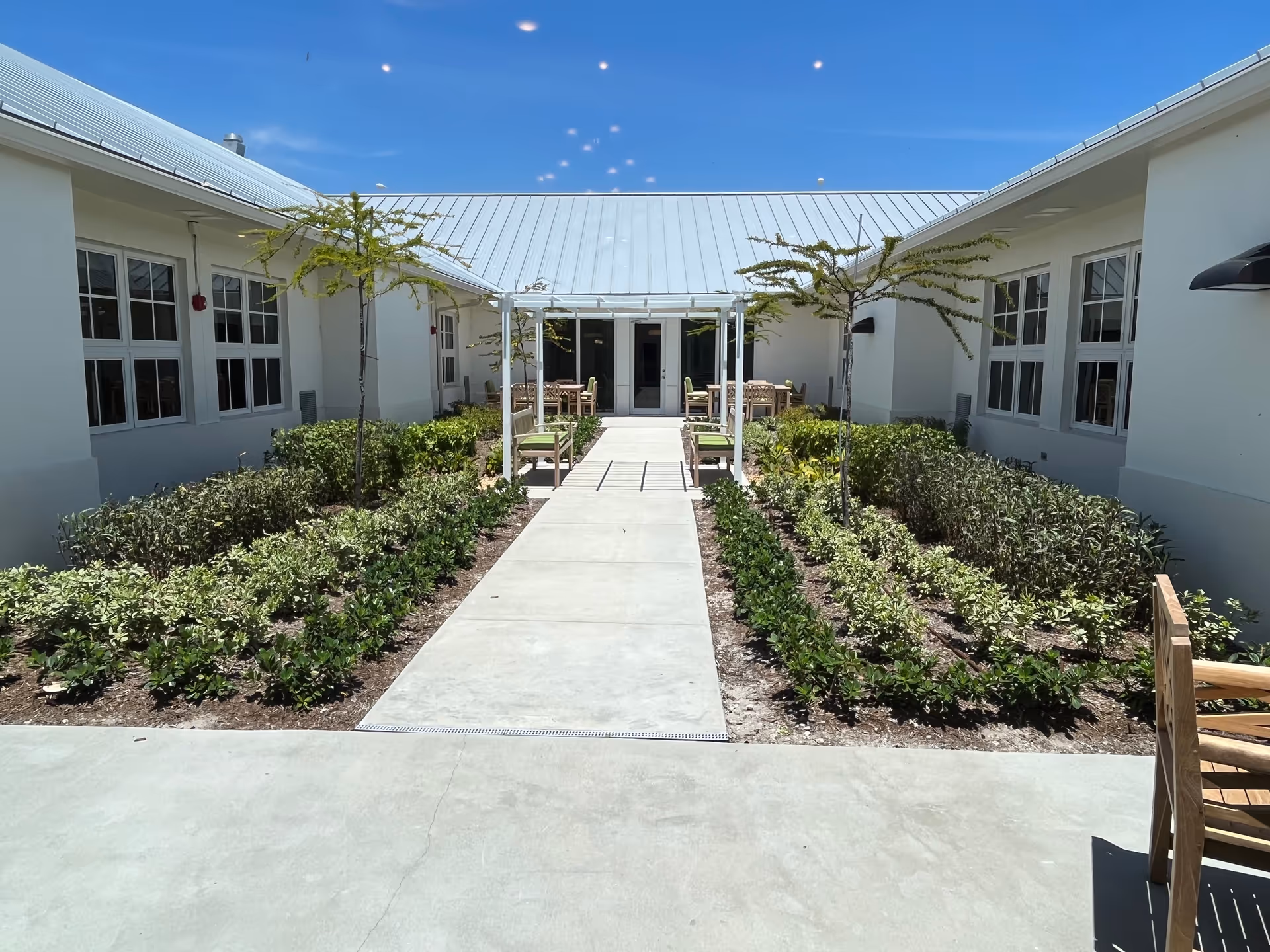 Bright outdoor courtyard between white buildings with a central path and seating areas.