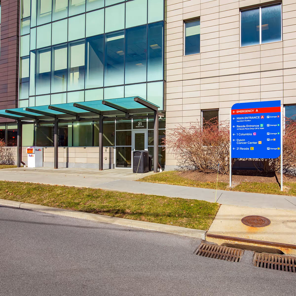 Modern building entrance with glass facade, green awnings, and a blue directional sign outside.