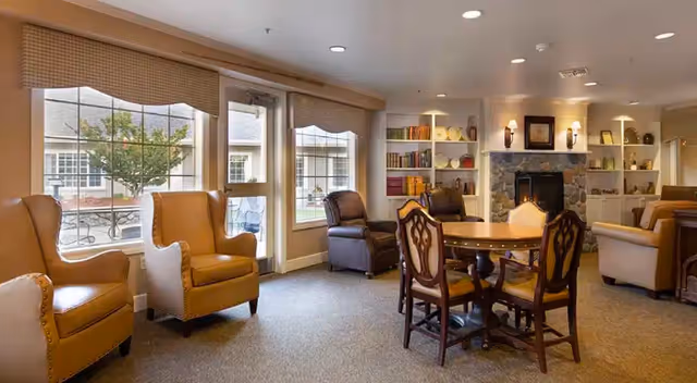 Cozy senior living lounge with chairs, table, bookshelves, and a fireplace.
