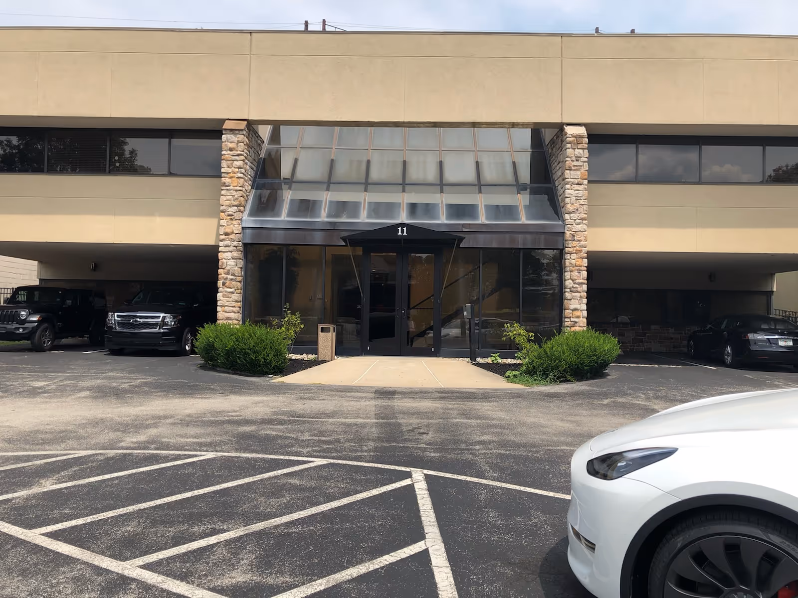 Modern senior living facility exterior with glass entry, stone pillars, and a parking lot.
