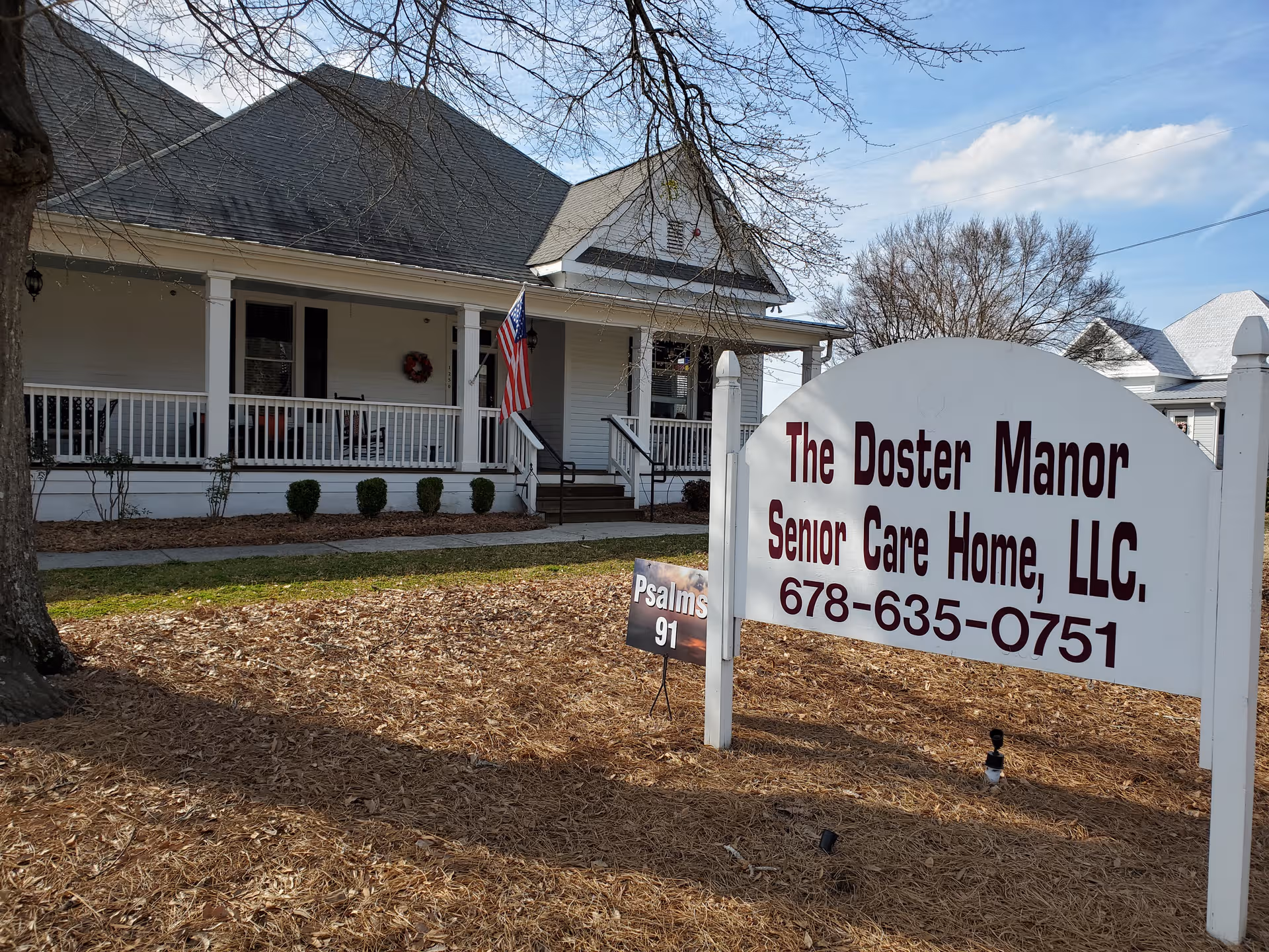 Front view of The Doster Manor Senior Care Home with a porch and sign.