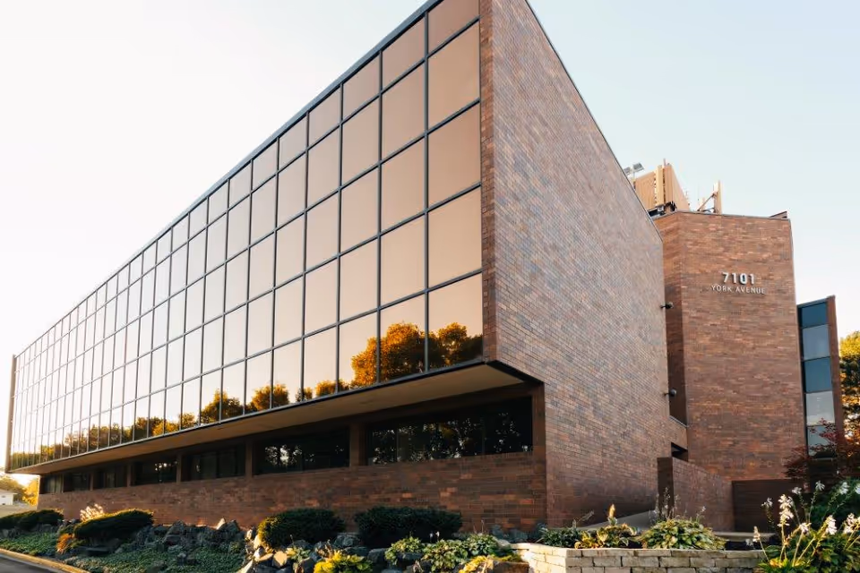 Exterior view of a modern brick building with large glass windows and landscaped front.